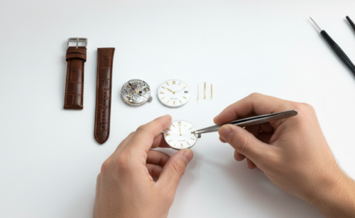 Person working on a watch with tools and components on a white surface